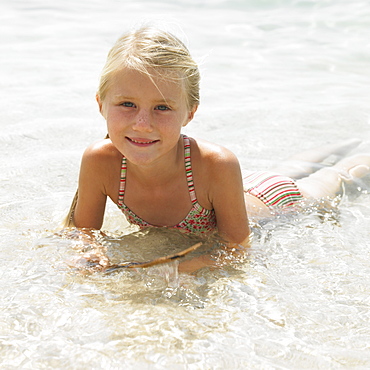 Girl (6-8) on beach lying in the surf