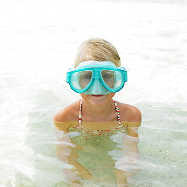 Girl (6-8) on beach wearing swimming mask in the surf