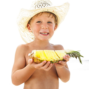 Boy (6-8) on beach holding slice of pineapple