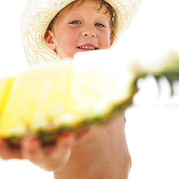 Boy (6-8) on beach holding slice of pineapple