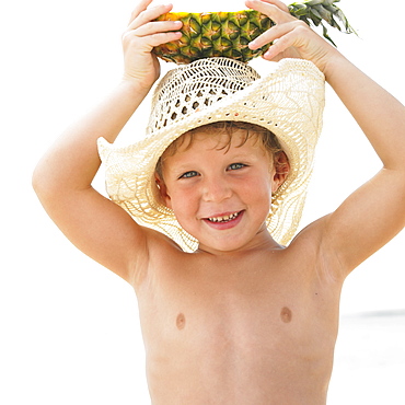Boy (6-8) on beach holding slice of pineapple