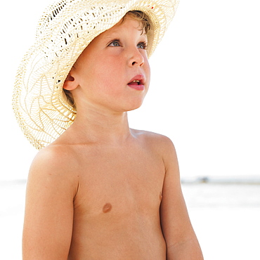 Boy (6-8) on beach wearing straw hat