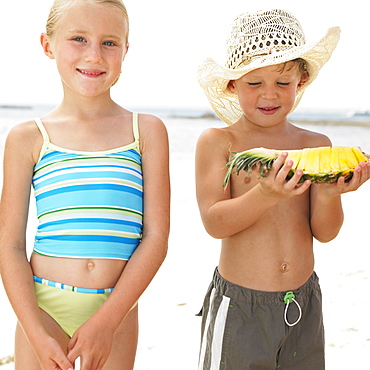 Boy and girl (6-8) on beach, boy holding slice of pineapple