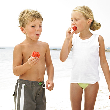Boy and girl (6-8) on beach eating watermelon