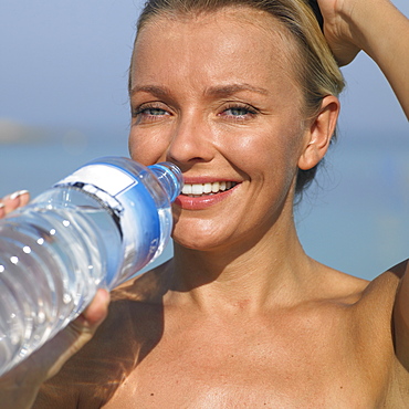 Woman drinking from water bottle on beach, close-up