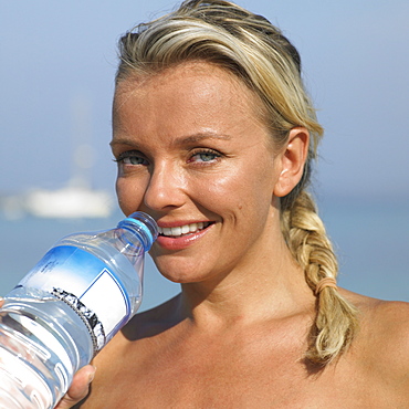 Woman drinking from water bottle on beach, close-up