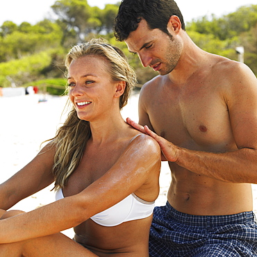 Man applying suncream to woman's back on beach