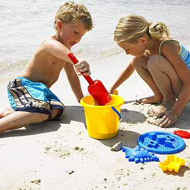 Boy and girl (6-8) on beach making sandcastles