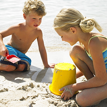 Boy and girl (6-8) on beach making sandcastles