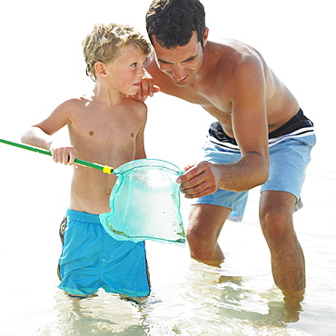 Father and son (6-8) in the surf holding fishing pole