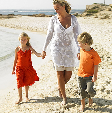 Mother and children (6-8) walking on beach