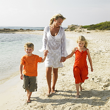 Mother and children (6-8) walking on beach