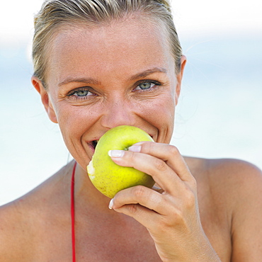 Woman in bikini on beach holding apple