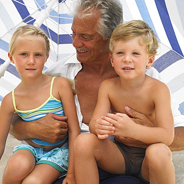 Grandfather and grandchildren (6-8) under parasol