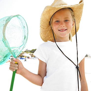 Girl (6-8) on beach wearing straw hat, carrying fishing pole