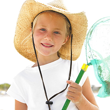 Girl (6-8) on beach wearing straw hat, carrying fishing pole