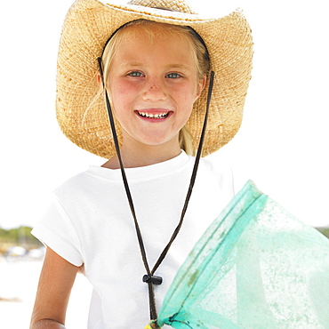 Girl (6-8) on beach wearing straw hat, carrying fishing pole