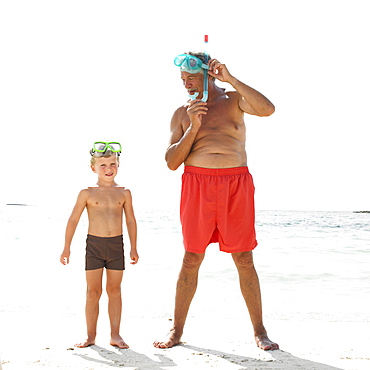 Grandfather and grandson (6-8) on beach with snorkelling masks