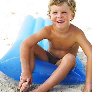 Boy (6-8) on beach sitting on inflatable air bed