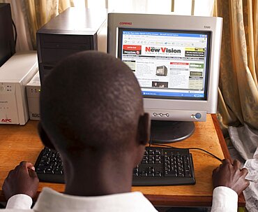 Uganda, Kabarole District, Fort Portal Teacher Training College Student teacher sat at a PC reading a National Newspaper