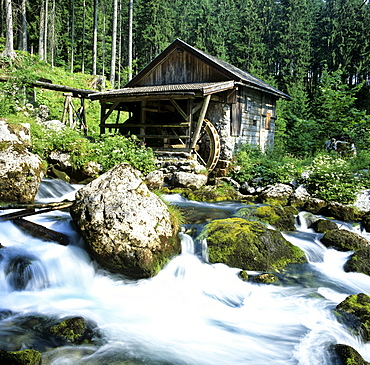 Watermill wheel beside a small waterfall in a mountain stream with moss-covered rocks