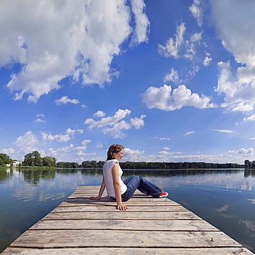 Girl relaxing on a pier of a quarry pond with a reflected cloudy sky, Ingolstadt, Bavaria, Germany, Europe