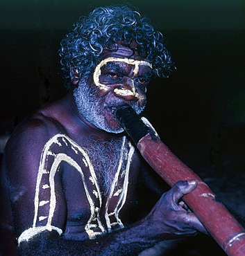 Aboriginal man with traditional decoration playing Didgeridoo on a dancing festivity