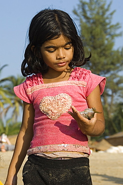 Young girl on the beach looking at a fish in her hand, Goa, India