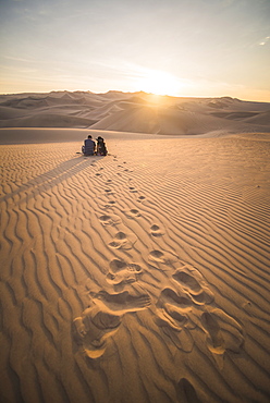 Couple watching the sunset over sand dunes in the desert at Huacachina, Ica Region, Peru, South America