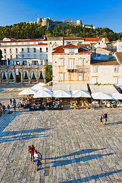 Tourists in St. Stephens Square, with the Spanish Fort (Fortica) above, Hvar Town, Hvar Island, Dalmatian Coast, Croatia, Europe 