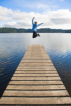 Woman jumping on a jetty at Lake Ianthe, West Coast, South Island, New Zealand, Pacific 