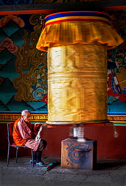 Portrait of elderly Buddhist monk turning prayer wheel, Punakha Dzong, Bhutan, Asia