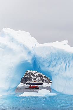 Lindblad Expeditions guests in a Zodiac as seen through an arch in an iceberg at Cierva Cove, Antarctica, Polar Regions