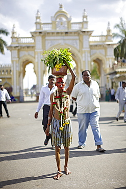 Pilgrim carrying holy water, gate to Amba Vilas Palace in background, Mysore, Karnataka, India