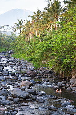 Father and son taking a bath in a river, riverbed, rocks, stones, local Balinese taking baths here, trees, local custom, intercu