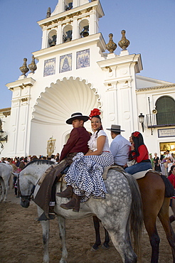 Couple on horseback in traditional dress in front of the church Eremita del Rocio at El Rocio at Pentecost, Huelva, Andalusien, Spanien