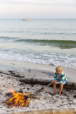 Five year old boy sitting around the campfire, adventure, sailing boat, dream beach between Strandmarken und Dueodde, sandy beach, summer, Baltic sea, Bornholm, Strandmarken, Denmark, Europe, MR