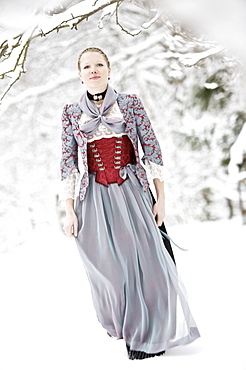 Young woman wearing a Dirndl standing in snowy scenery, Irsee, Bavaria, Germany