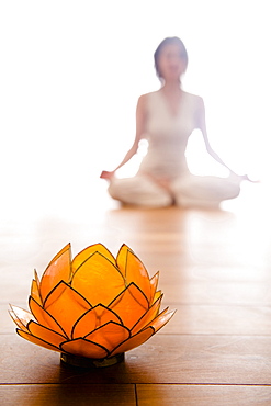 Mid adult woman practising yoga (Lotus pose), Lotus blosom in foreground, yoga studio at Linz, Austria