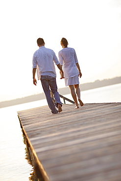 Couple walking hand in hand along jetty, Ambach, Lake Starnberg, Bavaria, Germany