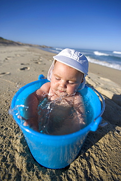 5 month old baby taking a bath in a bucket of Water on the beach, Nine Palms, Baja California Sur, Mexico