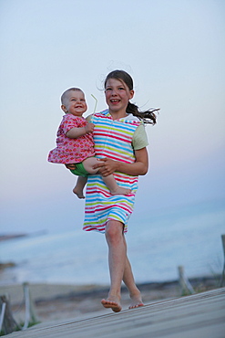 Girl carrying baby on jetty, Formentera, Balearic Islands, Spain