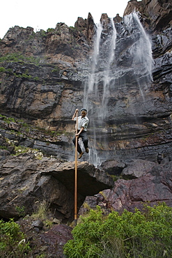 Man jumping with canarian crook in front of waterfall Cascada el Escobar, El Risco valley, Parque Natural de Tamadaba, Gran Canaria, Canary Islands, Spain, Europe