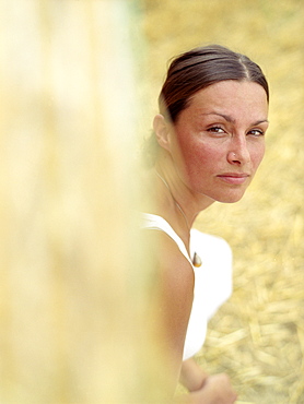 Woman looking along a bale of straw at camera, portrait