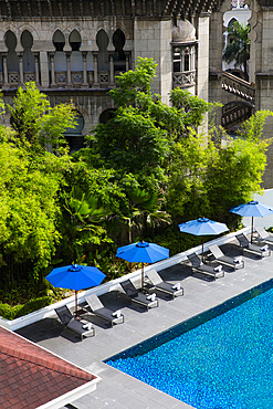 Pool with blue umbrellas, set against an old building and lush greenery. Kuala Lumpur, Malaysia.