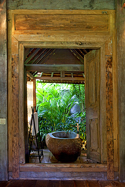 Stone bathtub set inside an open bathroom, in an old wooden house situated in the jungle. Bali, Indonesia.