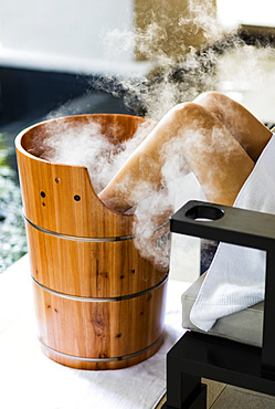 A woman having a footbath, in wooden barrel , with steam billowing. Horizontal. Kuala Lumpur, Malaysia.