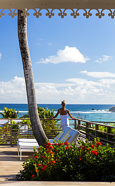 Woman in white, standing on a deck with her back to the camera, looking out onto the ocean. St. Barths.