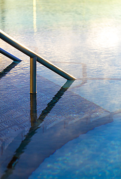 Detail shot of railing going into water in exterior pool, with morning steam. Bath, United Kingdom