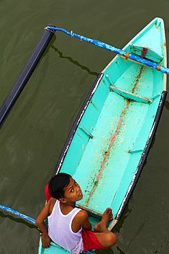 A young Malaysian boy looking into the camear from his turqoise boat, shot from above in Borneo, malaysia.